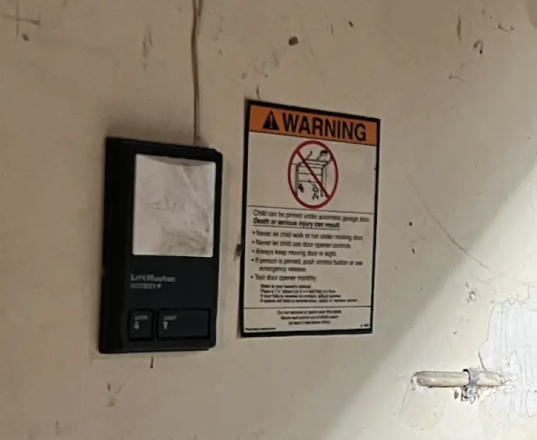 Garage door button on the wall inside the garage, next to a warning sign.