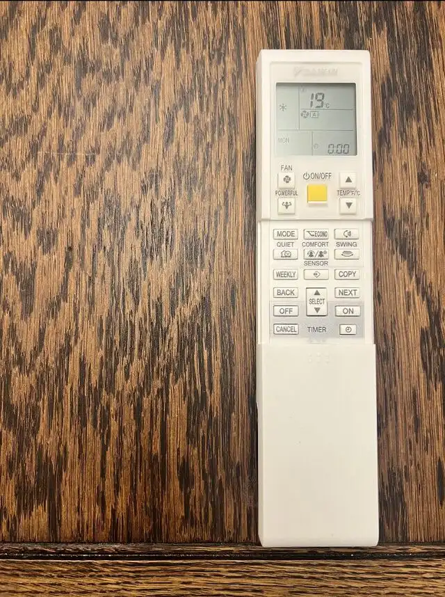 White air conditioner remote control on a wooden table. The lower cover slides down to show more buttons.