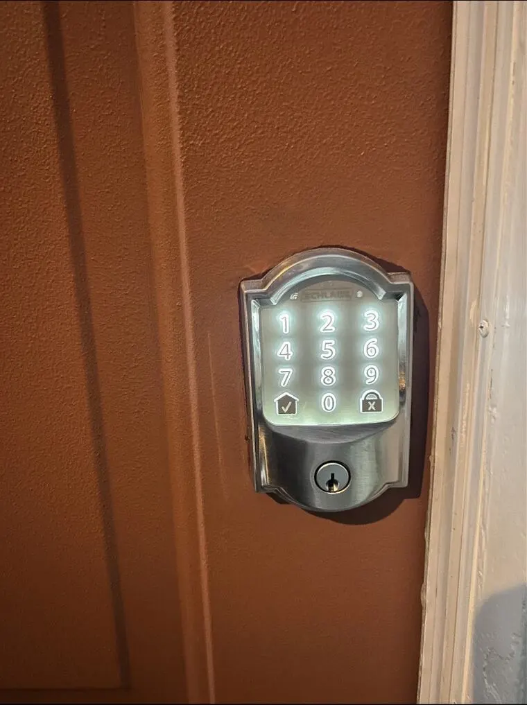 Touchscreen deadbolt on a red door. Step 1: press the checkmark at the lower left of the keypad. Step 2: enter the code on the number pad. Step 3: press the lock icon at the lower right to lock the door.